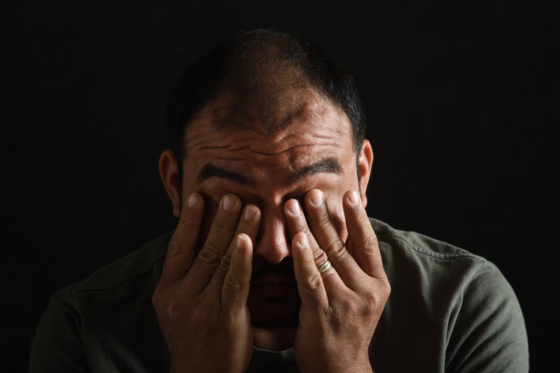 Tired and fatigued Latin American man holding his face in his hands